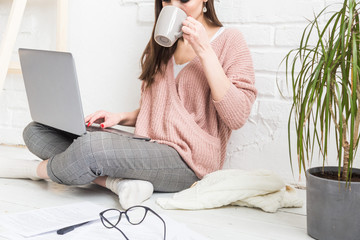 Young woman sits on the floor in a Scandinavian apartment interior with a laptop, studying law,...