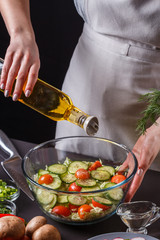 A young woman in a gray apron adds an oil to a Chinese cabbage salad
