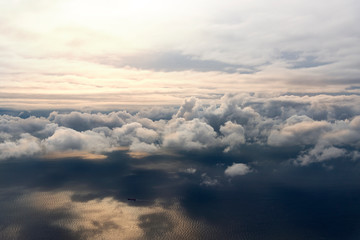 Clouds from a window of a commercial plane with sea and some ships over the sea.