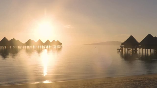 Travel vacation paradise sunset beach with overwater bungalows resort hotel in coral reef lagoon sea. 4K Video from Bora Bora, French Polynesia, Tahiti, South Pacific Ocean.