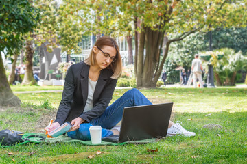 Young girl freelancer works with a laptop outdoors in the park. The concept of freelance work of the manager, remote business management