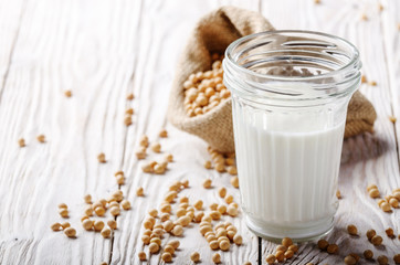 Non-dairy alternative Soy milk or yogurt in mason jar on white wooden table with soybeans in hemp sack
