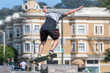 A skate boarder flies off the ramp at the Stanyan Skatepark in San Francisco near the end of Haight Street.  Victorian buildings in the background.  Sunny day.