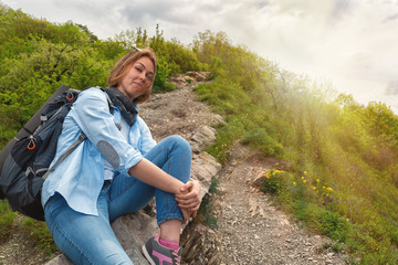 Naklejka na ściany i meble A young Woman sitting on a mountain stone path and posing for the camera. Sun light. Bottom view