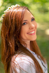 Naklejka premium Young beautiful girl with perfect skin and makeup is posing in a spring park scenery, looking at the camera. Gorgeous woman outdoors enjoying nature. Healthy smiling girl over a green background