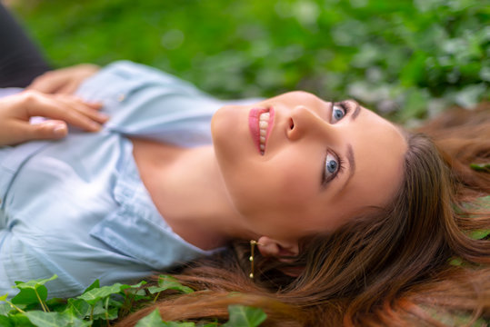 Young beautiful girl with perfect skin and makeup is lying down on ivy meadow, in spring park scenery, looking at the sky. Gorgeous woman outdoors enjoying nature. Healthy lady on green background