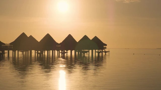 Resort hotel in travel vacation paradise at sunset beach with overwater bungalow in ocean lagoon with coral reef sea. 4K Video from Bora Bora, French Polynesia, Tahiti, South Pacific Ocean.