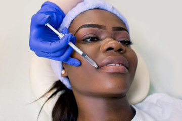 Young African woman getting lip injection in beautician salon, closeup