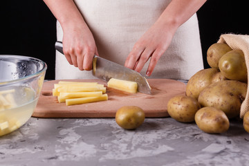 young woman in an apron cuts potatoes