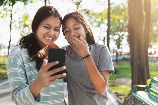 Asian mother and daughter feel relaxed While playing mobile phones, walking in the park in the morning