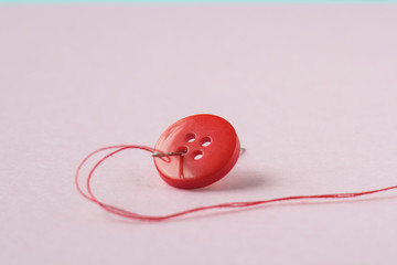 Red button, red thread and needle close up.