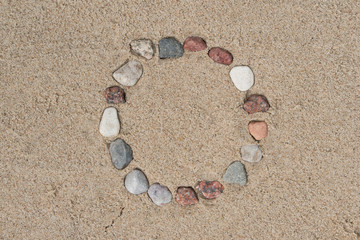 Fototapeta na wymiar round frame made of pebble stones on sand background