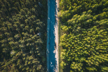 Fototapeta premium Aerial top view of asphalt road between green summer forest at sunny summer day