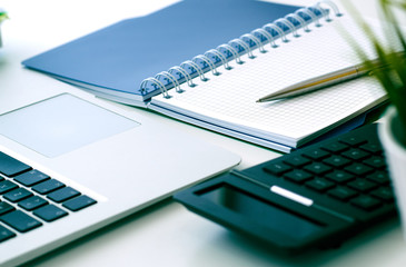 Closeup of white desktop with laptop, coffee cup, notepads, pen, calculator and other items.