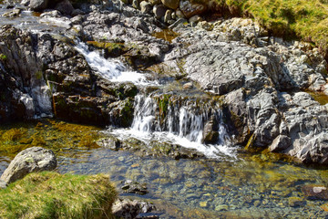 Stream leading out to small waterfall. Slow shutter speed. Bright sunny day. Grisedale pike, Lake District, England, UK