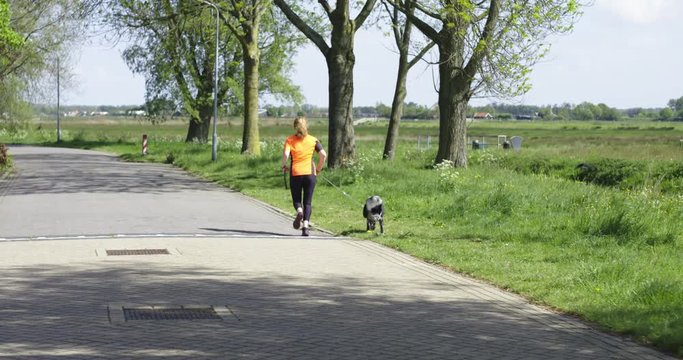 Young woman with young dog and orange shirt running / jogging towards camera in rural area.   