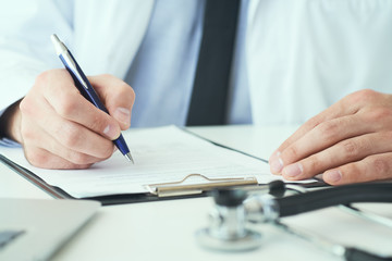 Mid section of male doctor writing write prescription to patient at worktable. Panacea and life save, prescribing treatment.