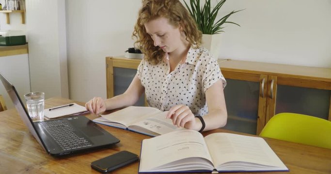 Young studen, blonde woman studying and working behind laptop, with books and notepad