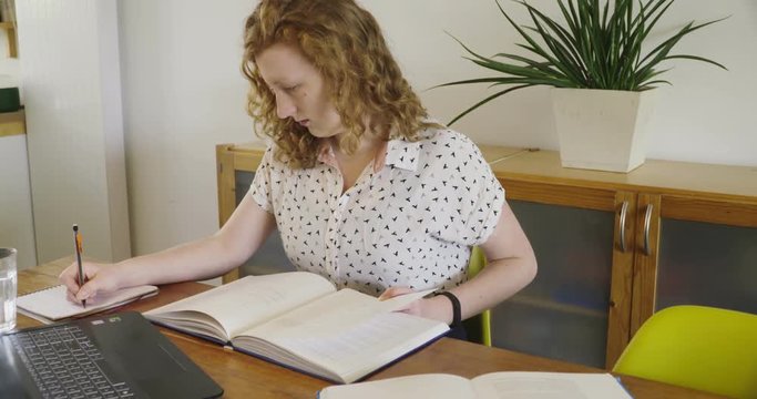Young studen, blonde woman studying and working behind laptop, with books and notepad