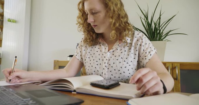 Young studen, blonde woman studying and working behind laptop, with books and notepad