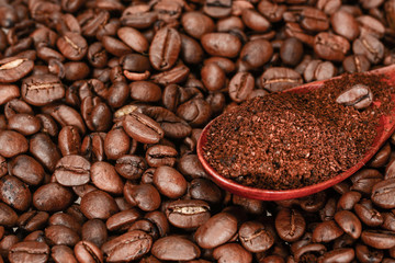 Brown bamboo spoon with ground coffee, lies on roasted coffee beans, close up.