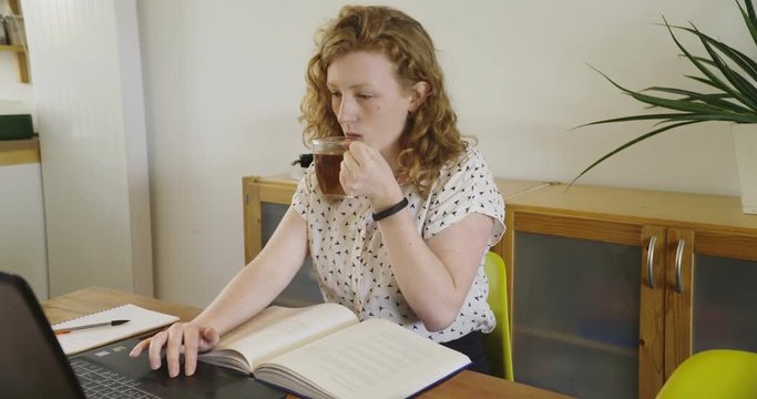 Young studen, blonde woman studying and working behind laptop, with books and notepad