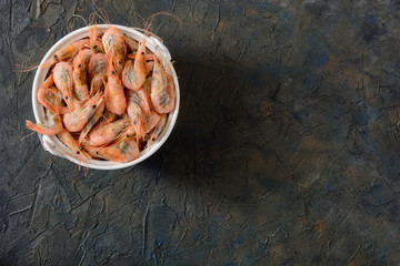 Frozen shrimps prepared for thawing in a deep bowl are on a dark background, top view, free space