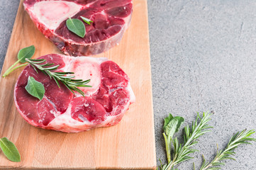 Sliced meat on a wooden board with herbs and spices. Raw meat on the bone close-up. Gray background. Copy space.