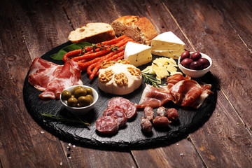 Cutting board with prosciutto, salami, cheese,bread and olives on dark stone background