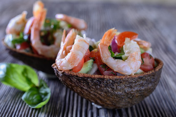 Appetizing salad of various fresh vegetables, avocado, garnished with shrimps on top is in the avocado peel as a portion salad bowl
