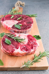 Sliced meat on a wooden board with herbs and spices. Raw meat on the bone close-up. Gray background.
