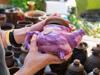Close up of woman hands with purple handmade ceramic kettle at art souvenir market. Handicraft,...