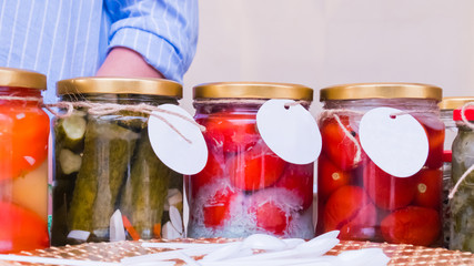 Homemade pickled tomatos and cucumbers jars with empty white label at outdoor market. Mock up, copyspace, template and street market concept