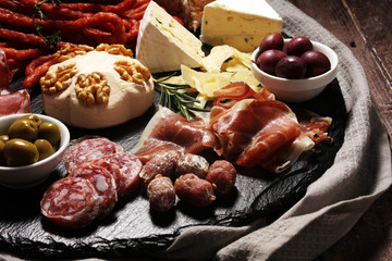 Cutting board with prosciutto, salami, cheese,bread and olives on dark stone background