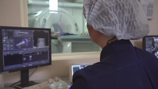 Doctor looking at computer screen while patient moving in mri machine