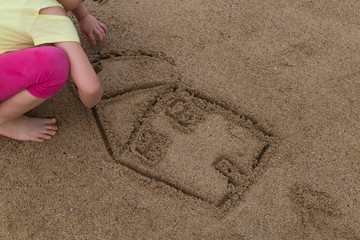the child draw house picture on the sand at the beach by the sea in the summer for holiday concept.