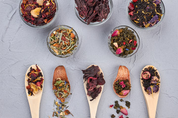 Dry tea assortment. Various dry tea in bowls and wooden spoons on gray background. Food concept.