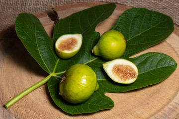 two fresh green figs and one fig cut in half displayed on a fig leaf