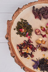 Assortment of dry tea on tree slice, top view. Round wood stand with assorted dry tea, top view. Ingredients for healthy drink.