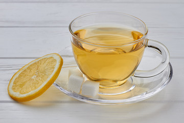 Cup of tea and slice of lemon. Transparent cup of tea with lemon slice on white wooden background. Delicious herbal beverage.