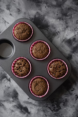 Tasty homemade chocolate muffins in baking tin on dark background top view