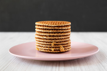 Stack of homemade Dutch stroopwafels with honey-caramel filling on a pink plate, side view.