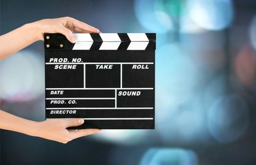 Cinema clapperboard in female hands on blue bokeh background