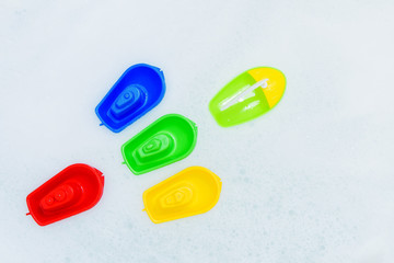 Plastic multicolored toy boats on foam bath.