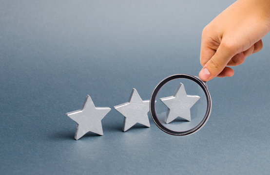 Magnifying Glass Is Looking At Three Stars On A Gray Background. The Concept Of Rating And Evaluation. The Rating Of The Hotel, Restaurant, Mobile Application. Quality Service, Buyer Choice. Success