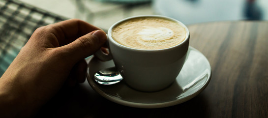 Holding the cup of coffee over the wooden table