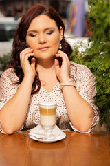 Lovely red haired middle-aged woman with curly hair sitting at the street cafe