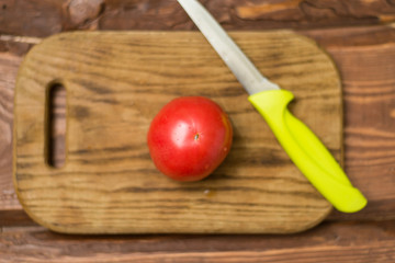 Fresh red tomato on a cutting wooden board with a knife.