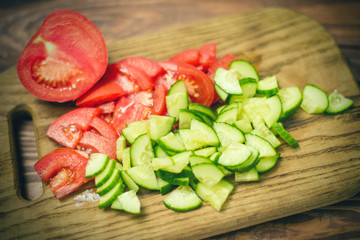 Sliced fresh tomato and cucumber on a wooden board. Cooking vegetable salad. The concept of healthy, vegan food.