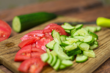 Sliced fresh tomato and cucumber on a wooden board. Cooking vegetable salad. The concept of healthy, vegan food.